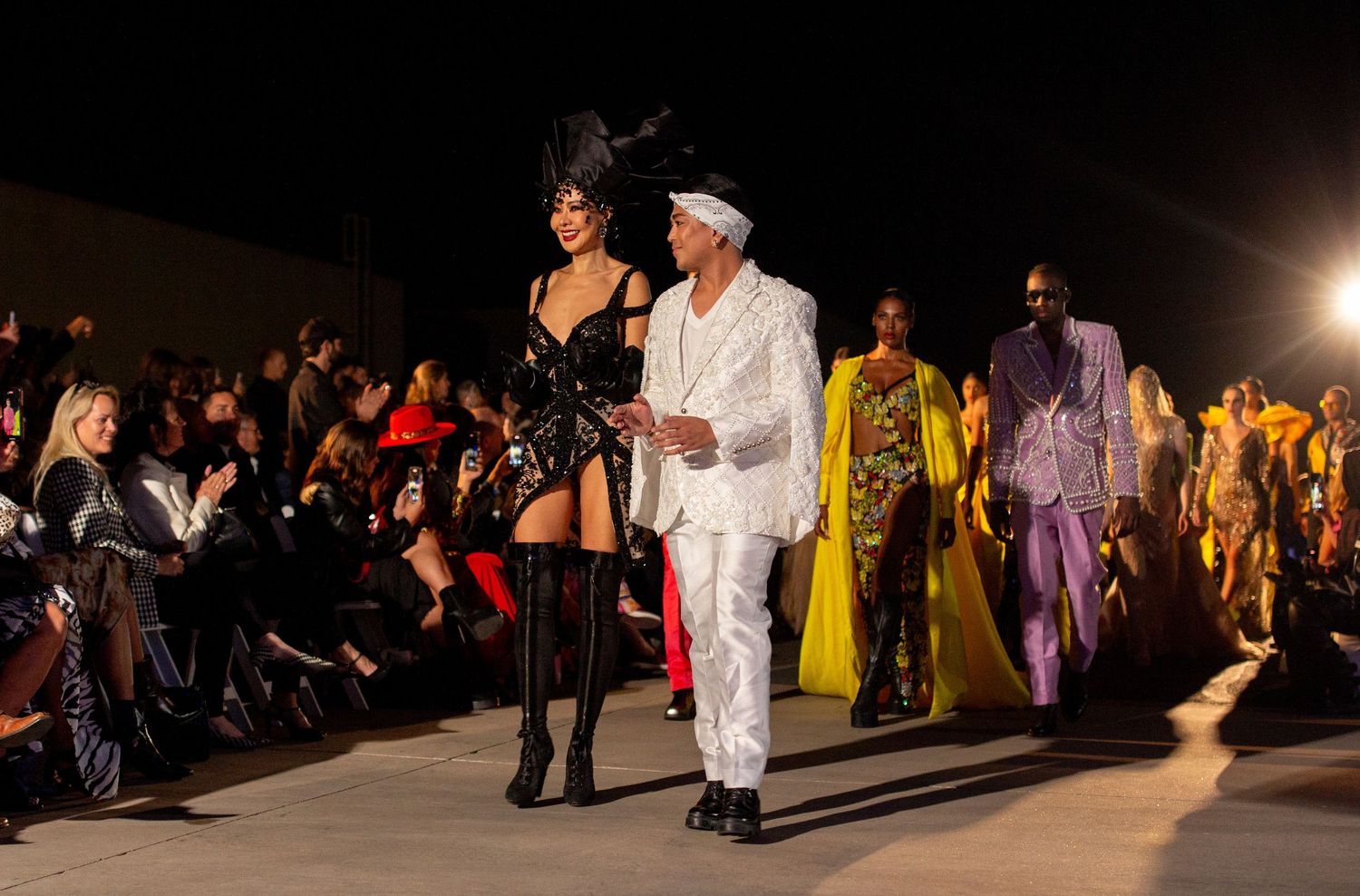 Designer geht mit mehreren Models über den Laufsteg während einer Outdoor-Fashion-Show.