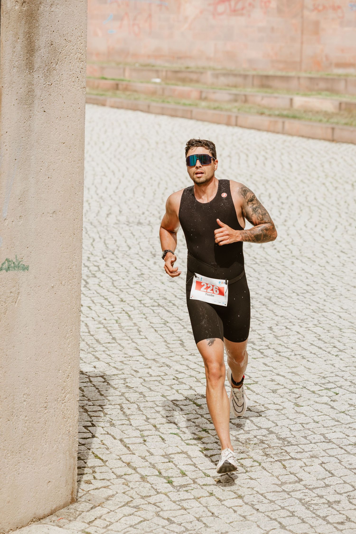 Triathlet läuft auf heller Pflasterfläche an einer Wand vorbei.
