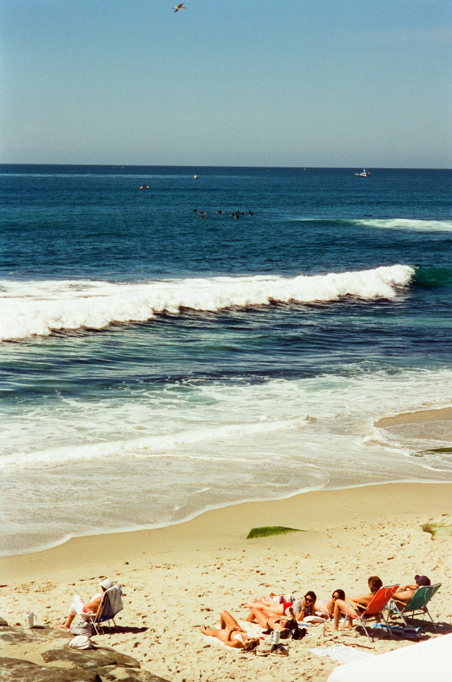 Blick auf Strand mit türkisfarbenen Wellen und Menschen, die im Wasser stehen.