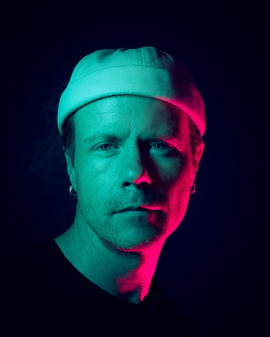 Artistic portrait with neon cyan and red lighting against dark background.