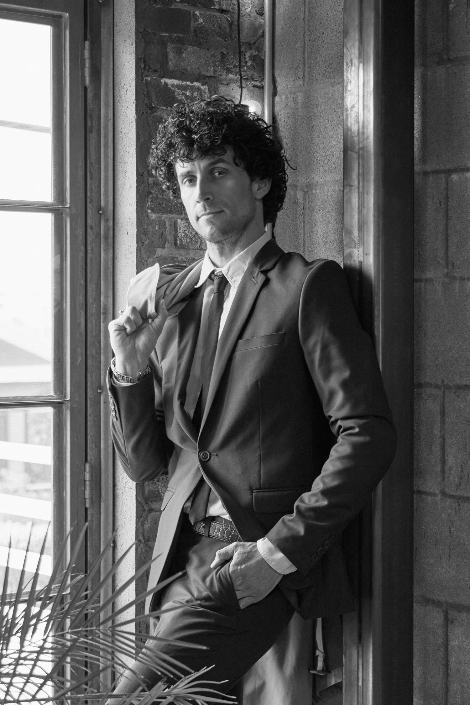 Black and white photos of person in suit posing by vintage windows.
