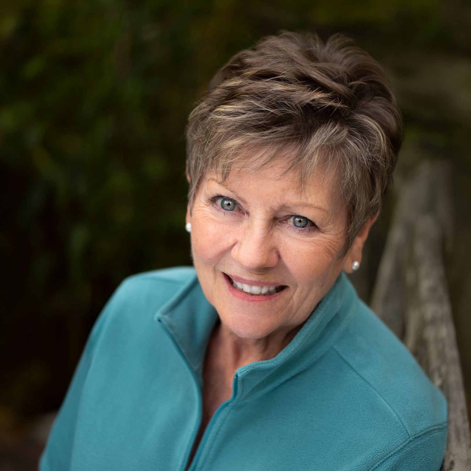 Professional headshot of someone wearing a teal colored top against a dark blurred background.