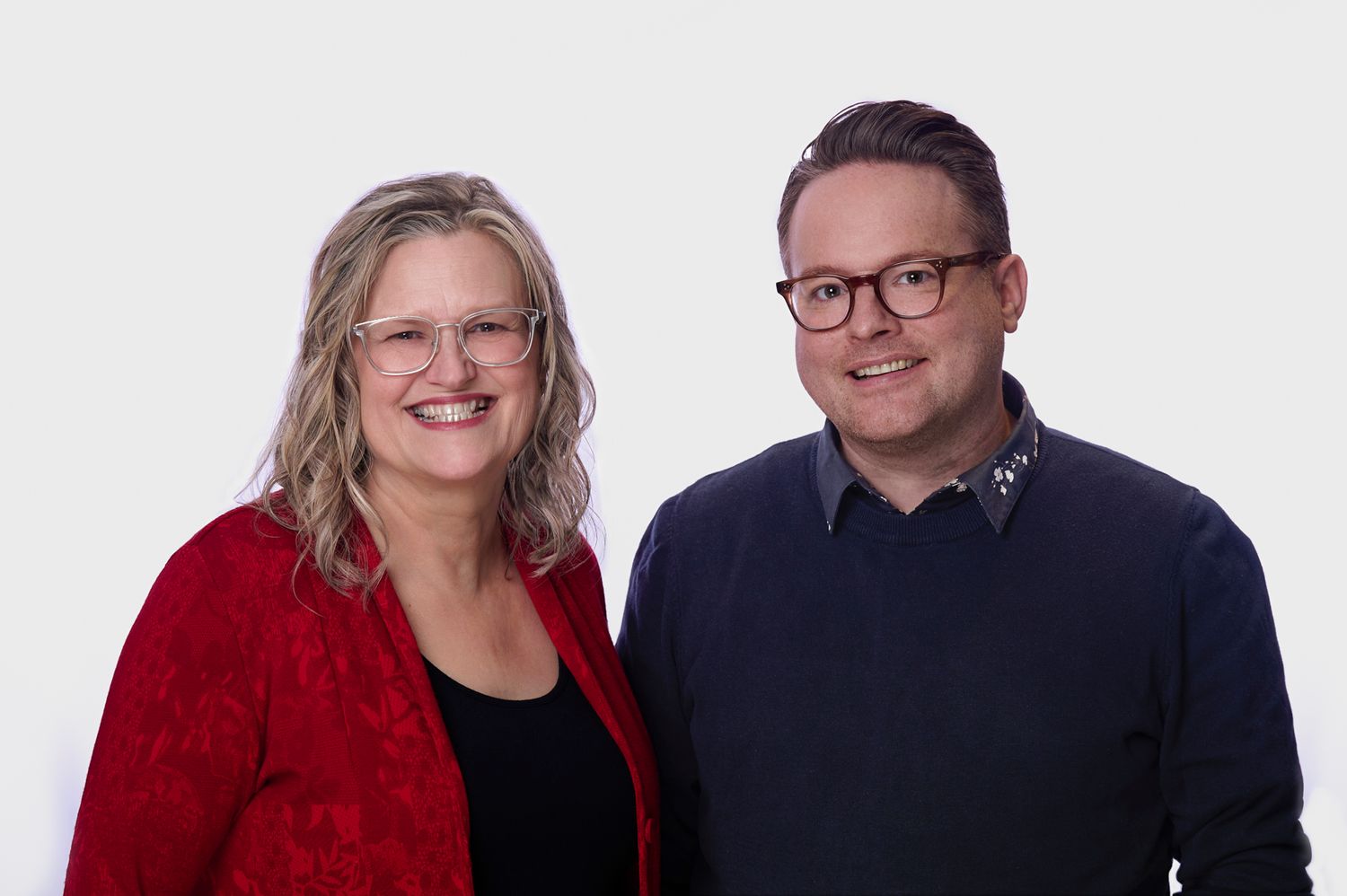 A couple wearing glasses poses together in a business photo with with white background.