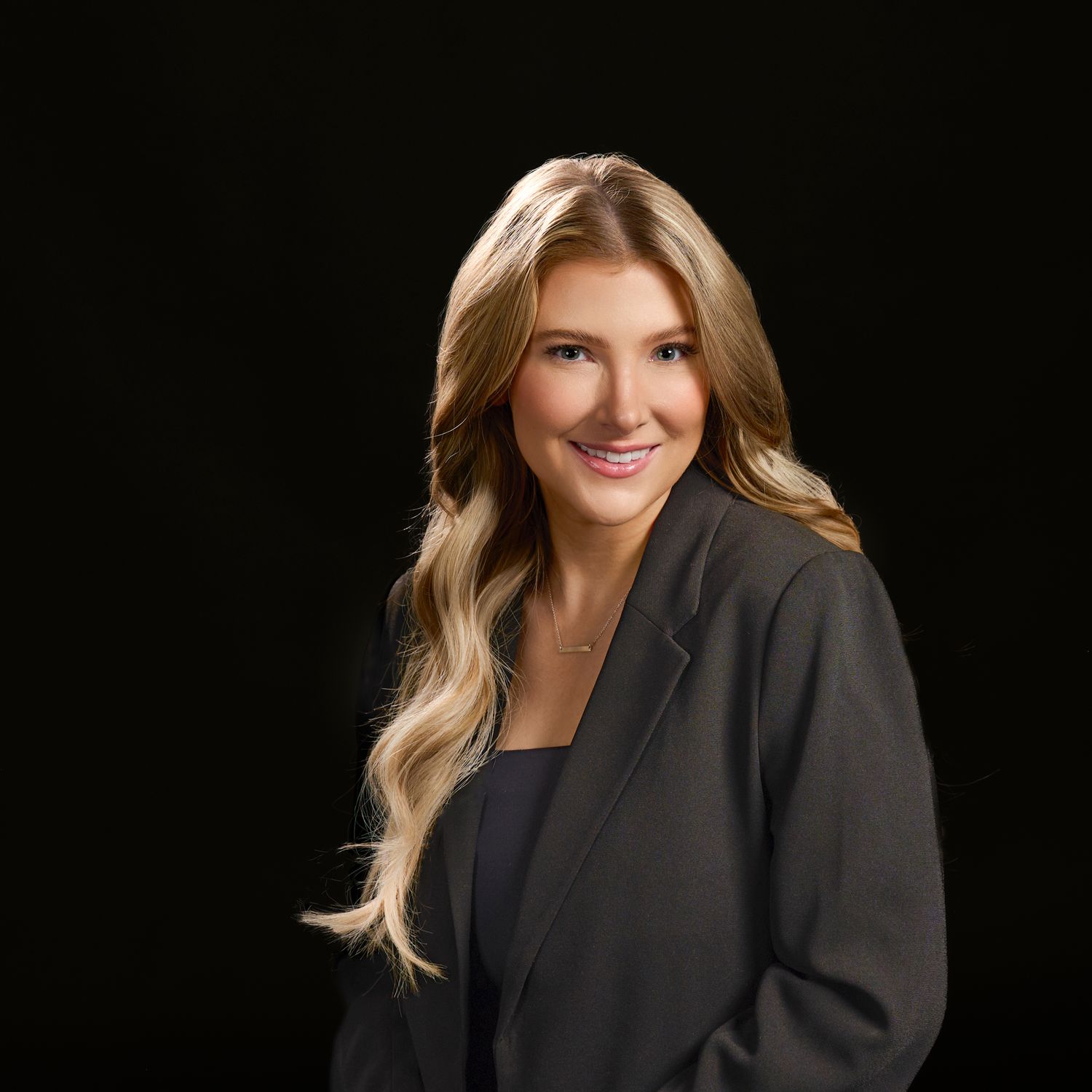Professional headshot of someone in a black blazer against a dark background with soft lighting.
