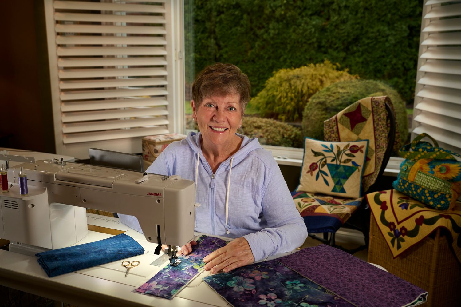 A person works on a colorful quilting project at a sewing machine in a bright home studio space.