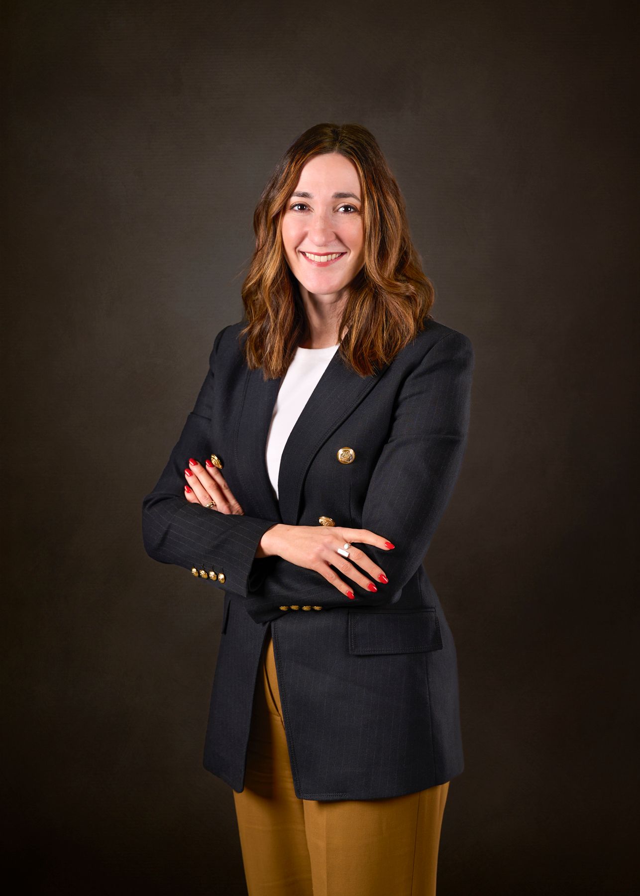 Professional portrait showing a person in a navy blazer and brown skirt against a dark background.