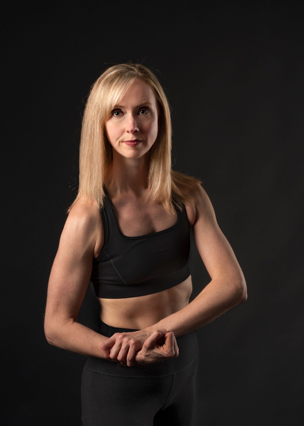A dramatic portrait of a fitness model in athletic wear against a dark background.