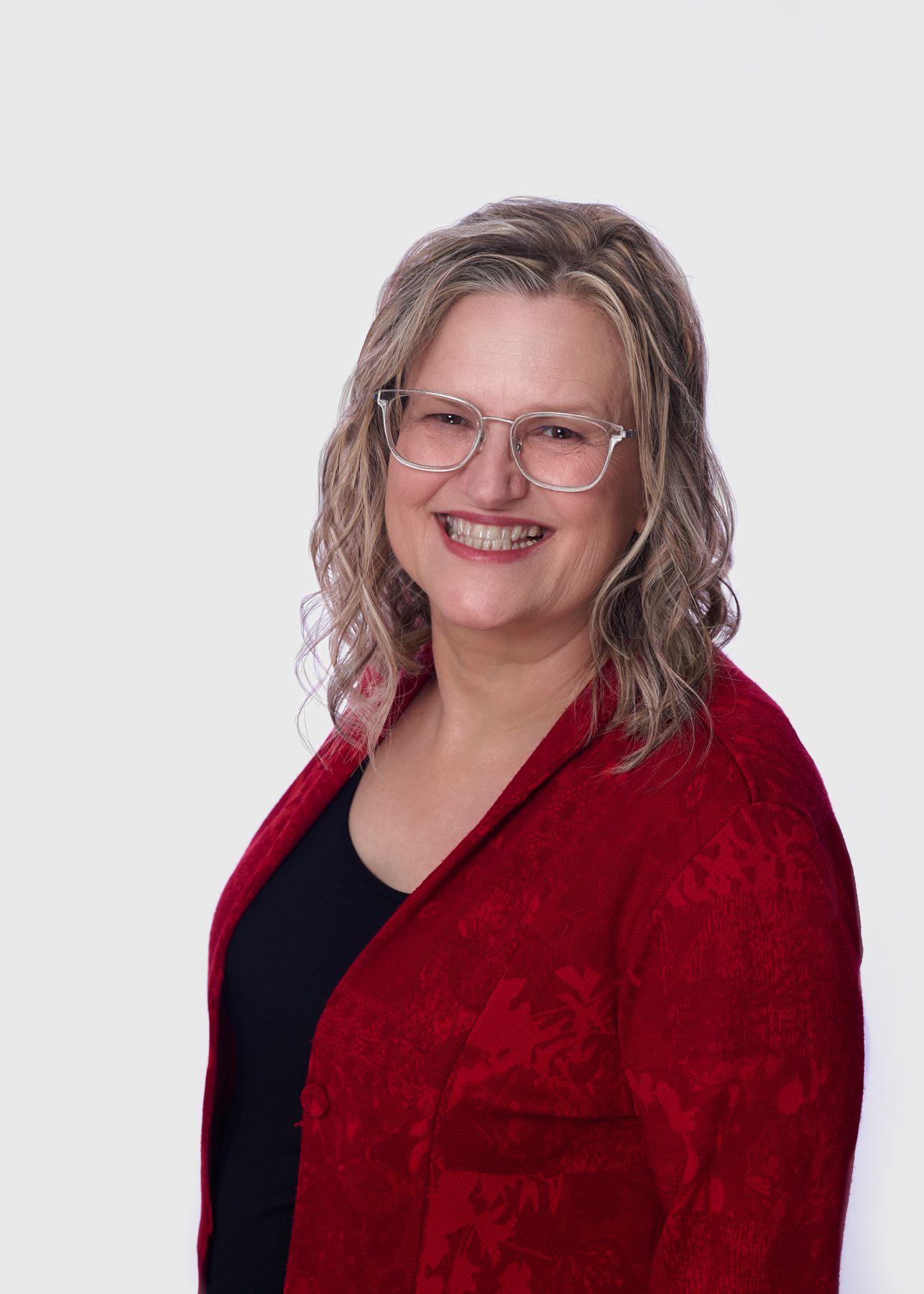 A person in a red blazer and black top poses in a professional headshots against a white background.
