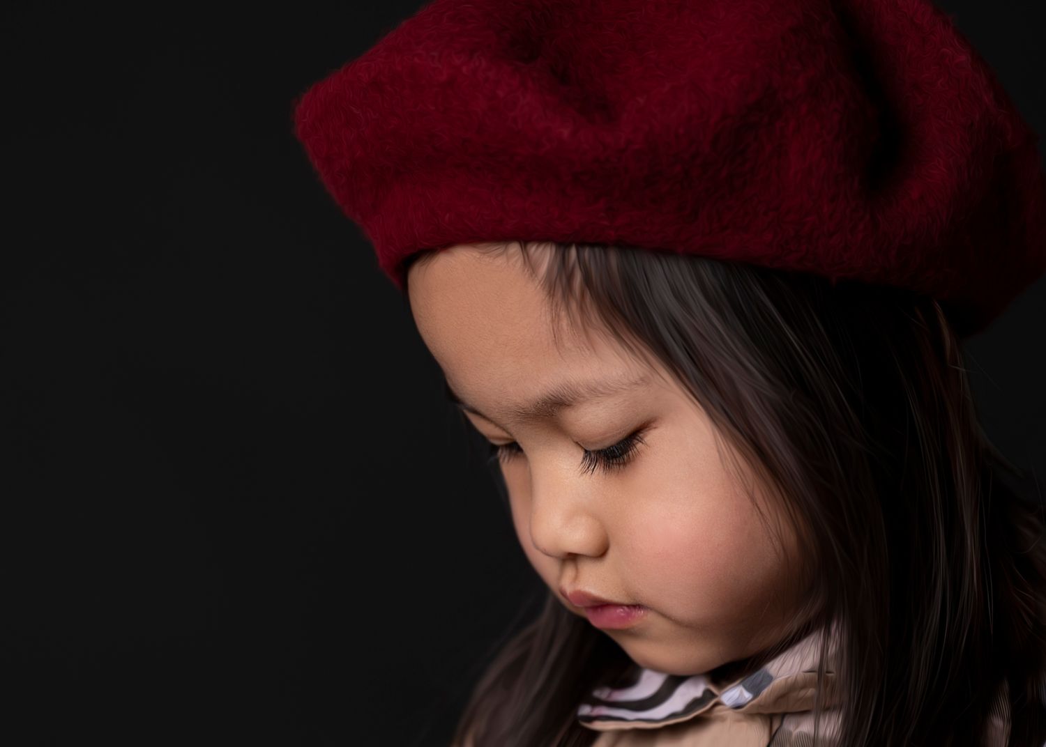 A young child in a red beanie hat looks down thoughtfully against a dark background.