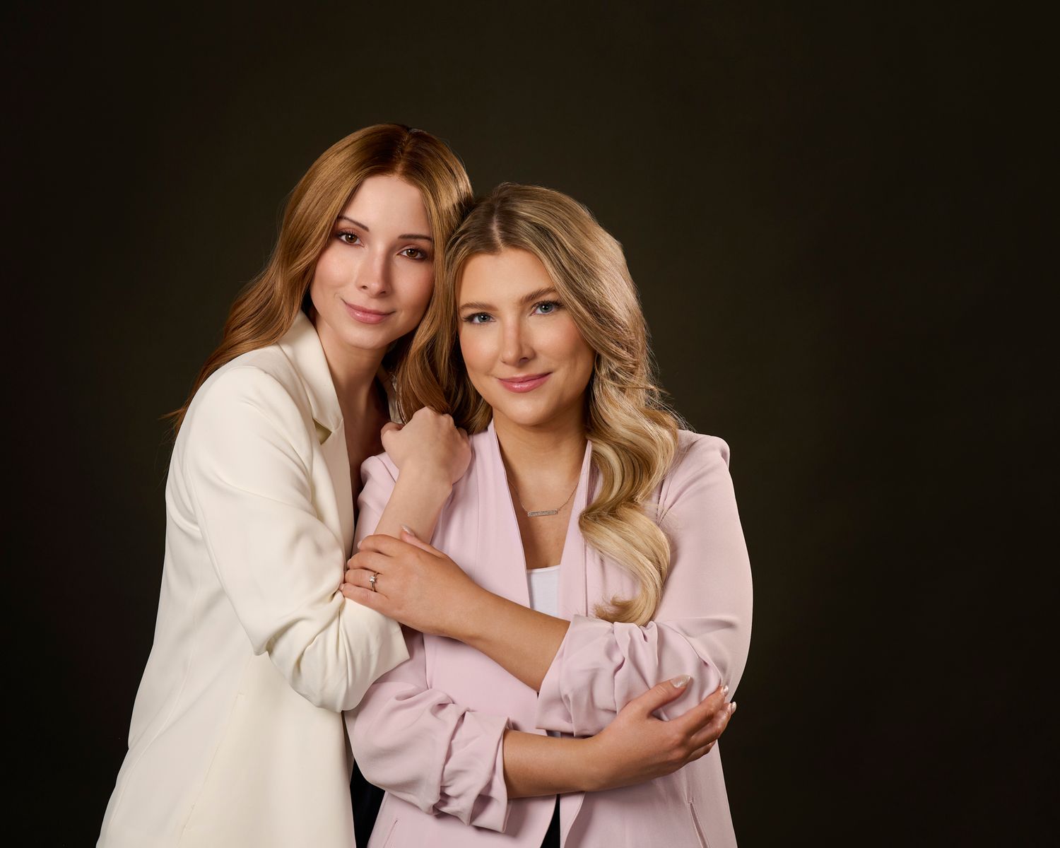Two people wearing light colored outfits pose together against dark backgrounds in a series of studio portraits.