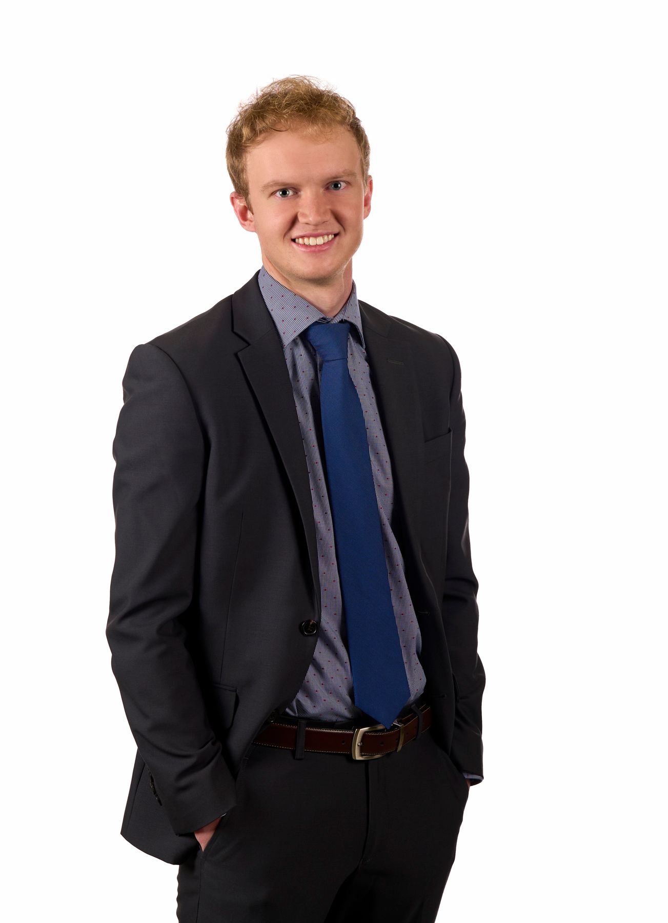 Professional portrait of someone in a dark business suit with blue tie against a plain background.