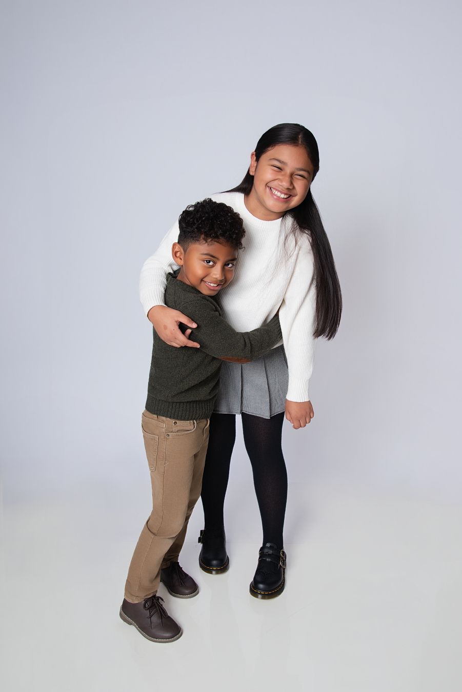 Two people share a warm embrace while standing against a light gray background.