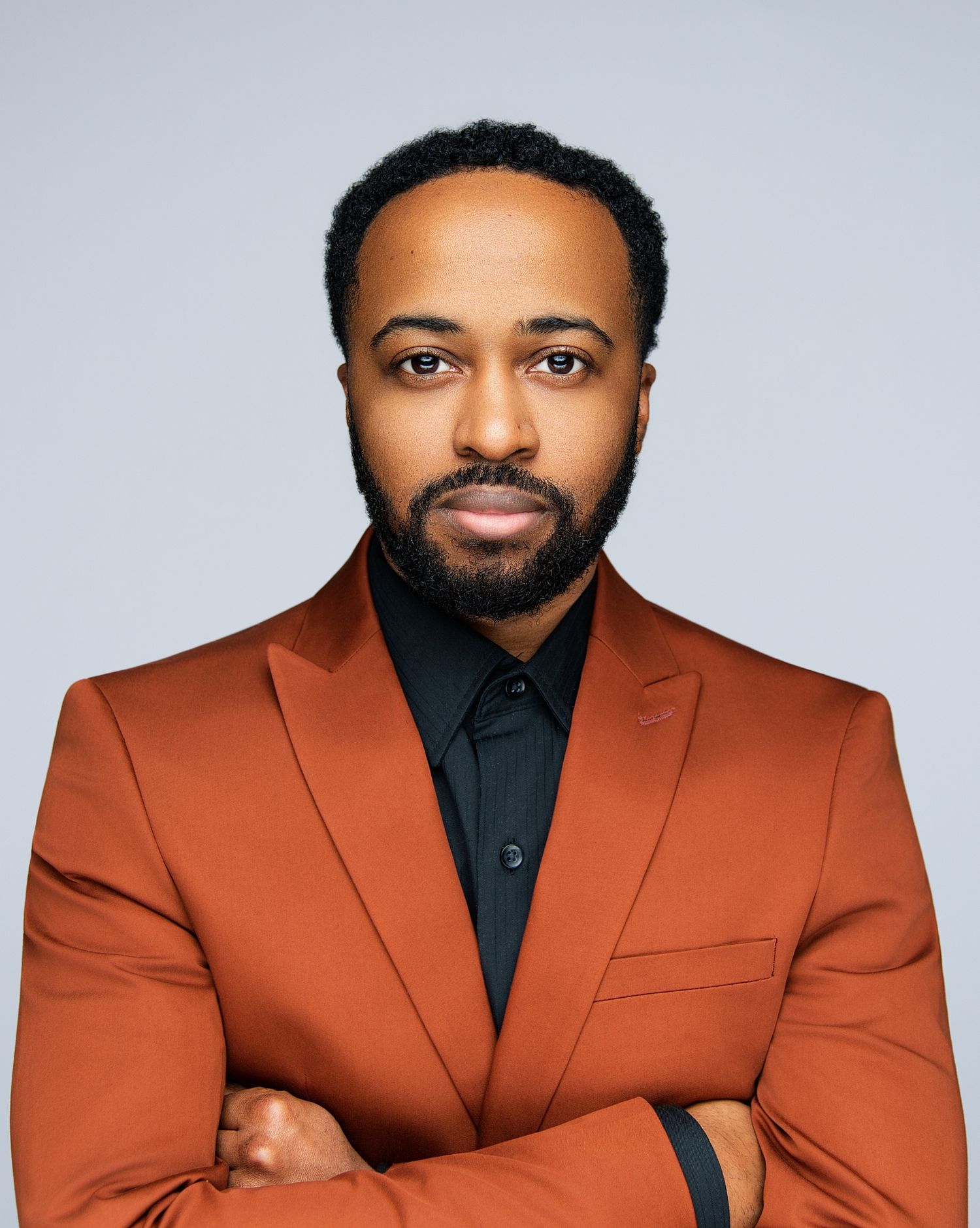 Professional studio portraits showing a person in a rust-colored suit jacket and black shirt against a light background.