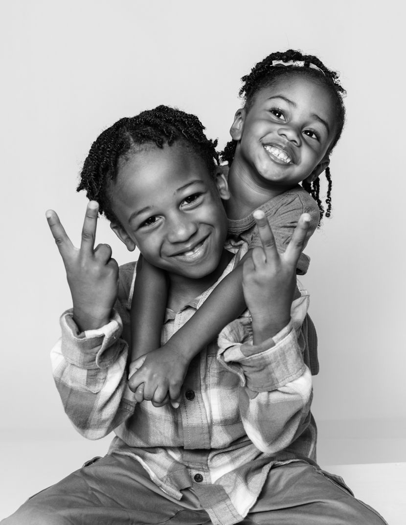 Two children posing playfully together in black and white portrait with bright smiles and hand gestures.