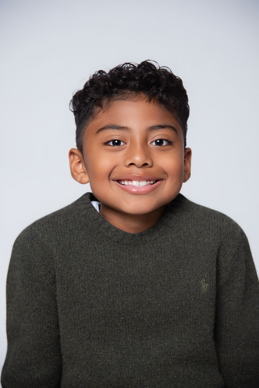 Young person wearing a dark green sweater smiles warmly against a light gray background.