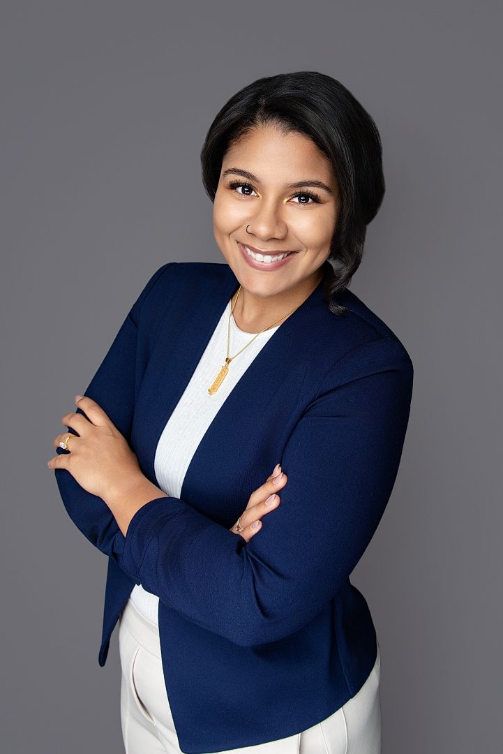 Professional woman in navy blazer smiling with arms crossed against gray background.