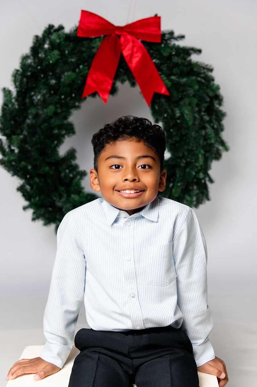 A series of holiday portraits with a green wreath and red bow against a light gray background.