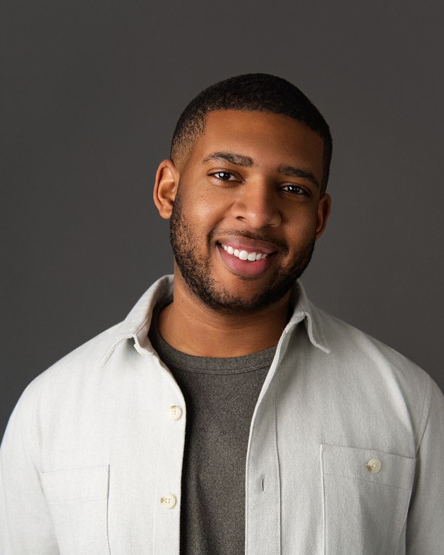 Professional studio portrait of someone wearing a white button-up shirt against a gray background.
