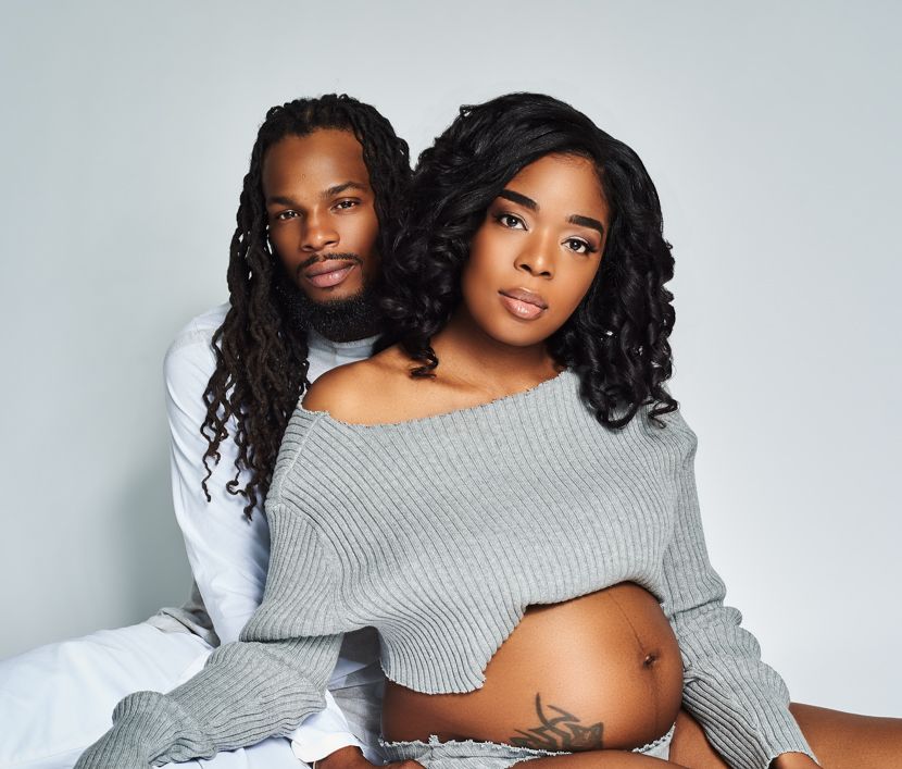 Maternity photo of couple in casual wear against light background.