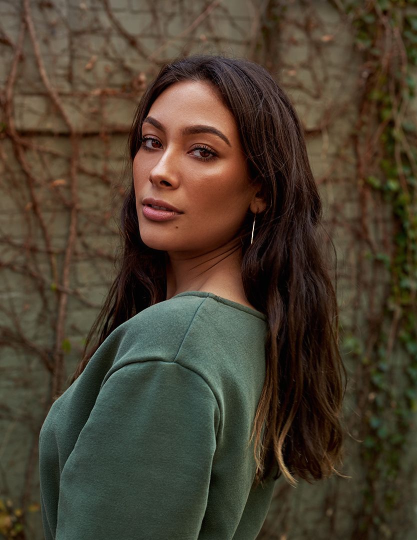 Fashion portraits of someone wearing a dark green sweater against a vine-covered wall.