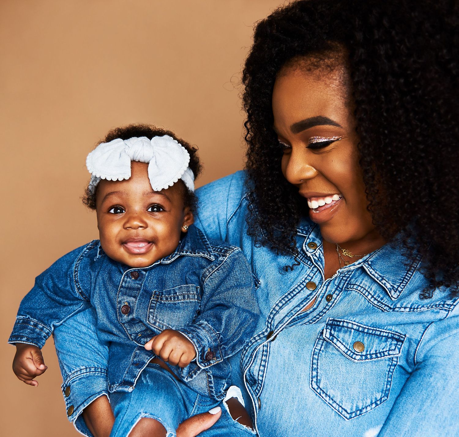 Parent and child in matching denim outfits share joyful laughter while playing together.
