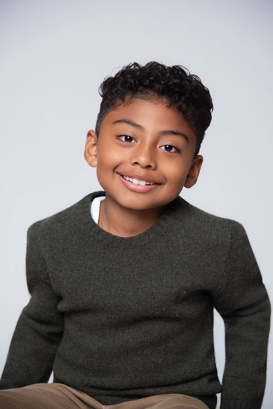 A child in a dark green sweater poses playfully against a light gray background in a series of four shots.