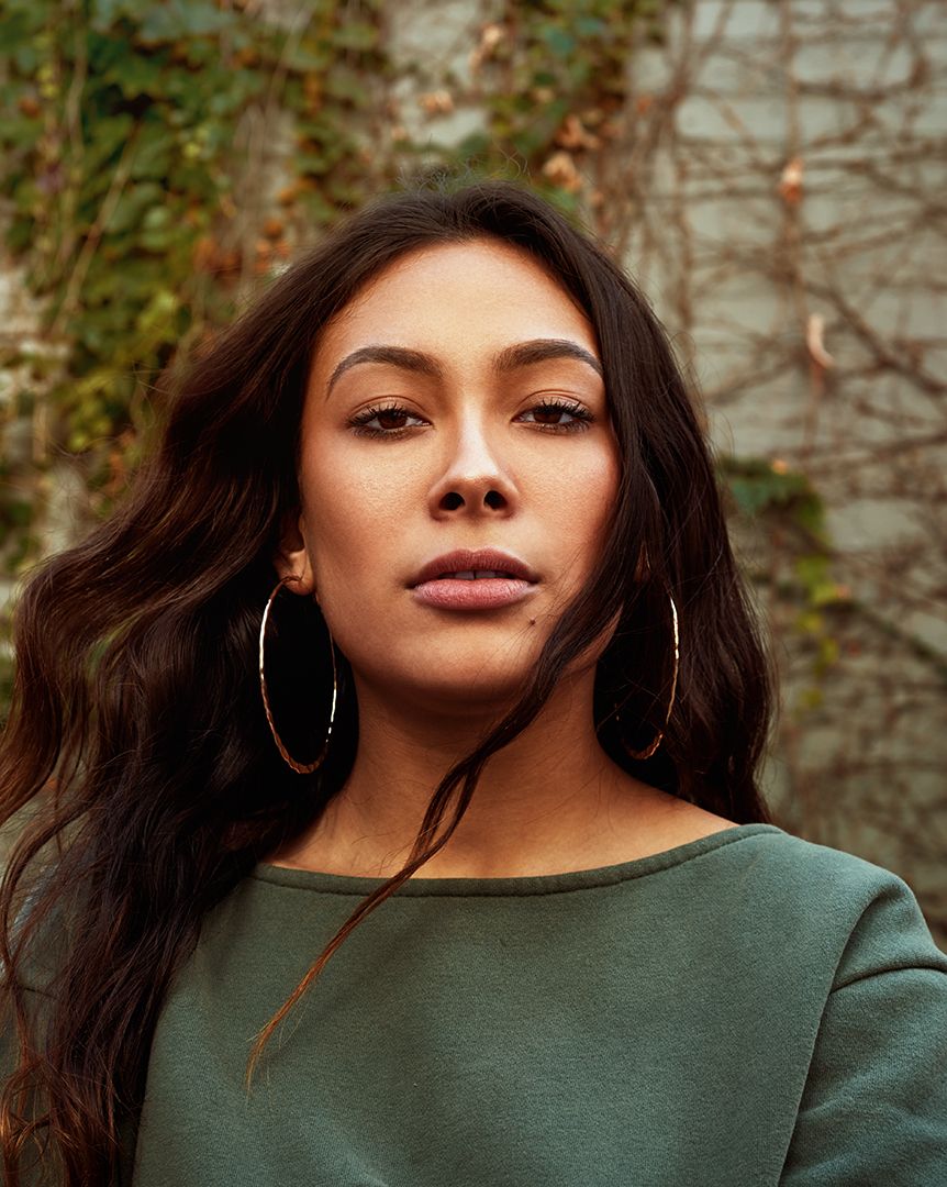 Close-up portrait of woman in green top with hoop earrings against natural background.