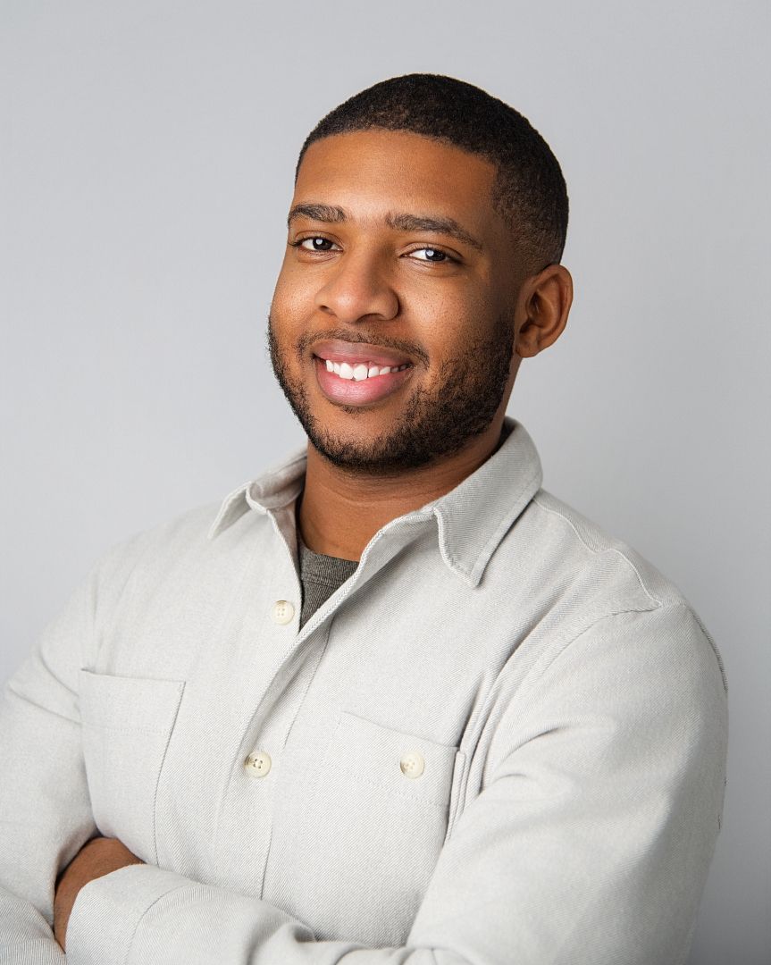 Professional headshot portrait of someone wearing a light colored sweater against a neutral gray background.