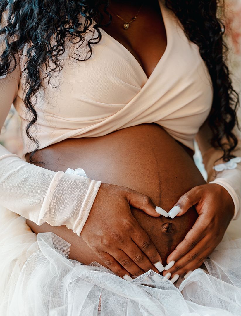 Maternity photo showing pregnant belly in white dress against floral backdrop.