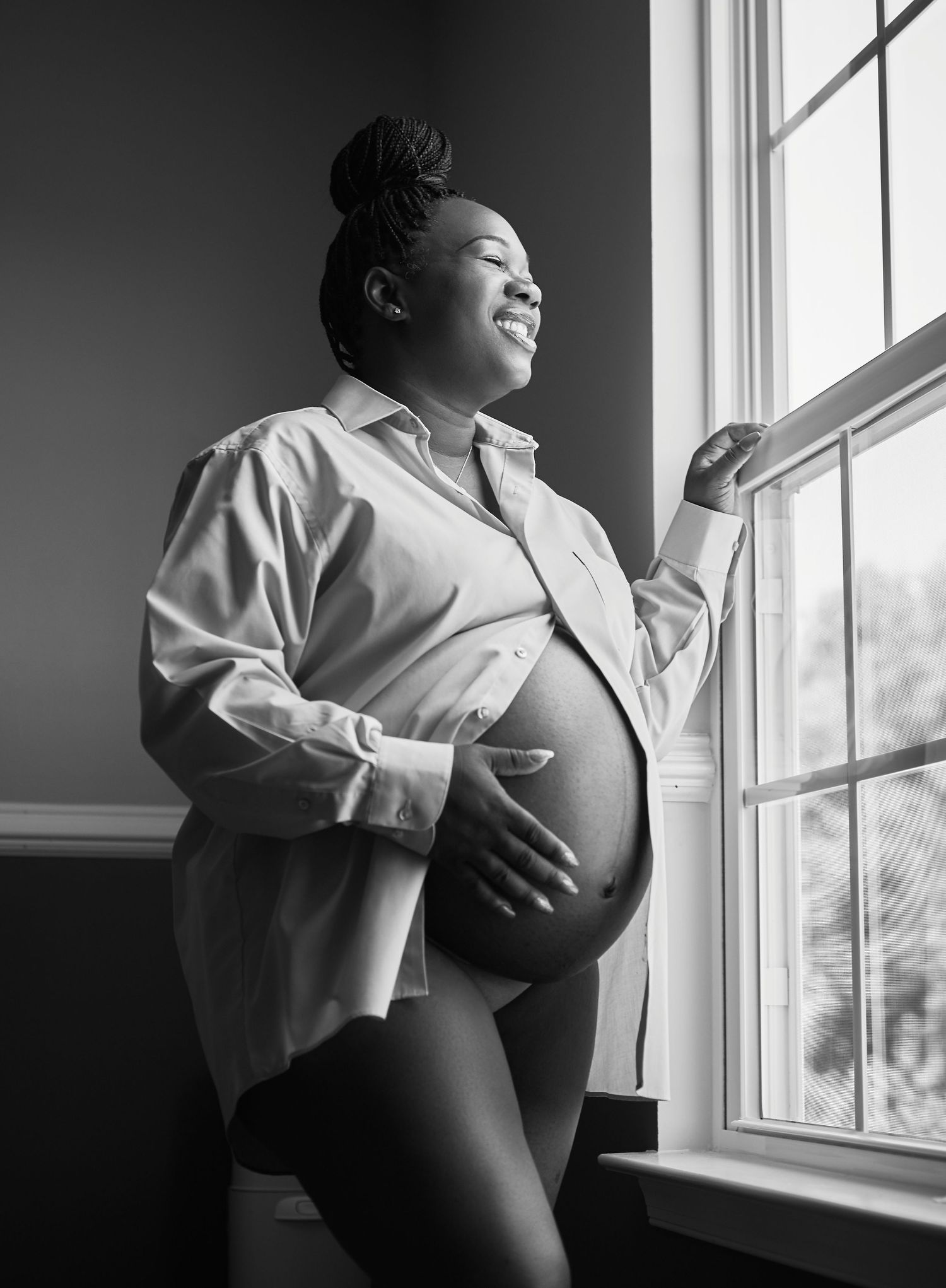 Dramatic black and white maternity portraits near a sunlit window.