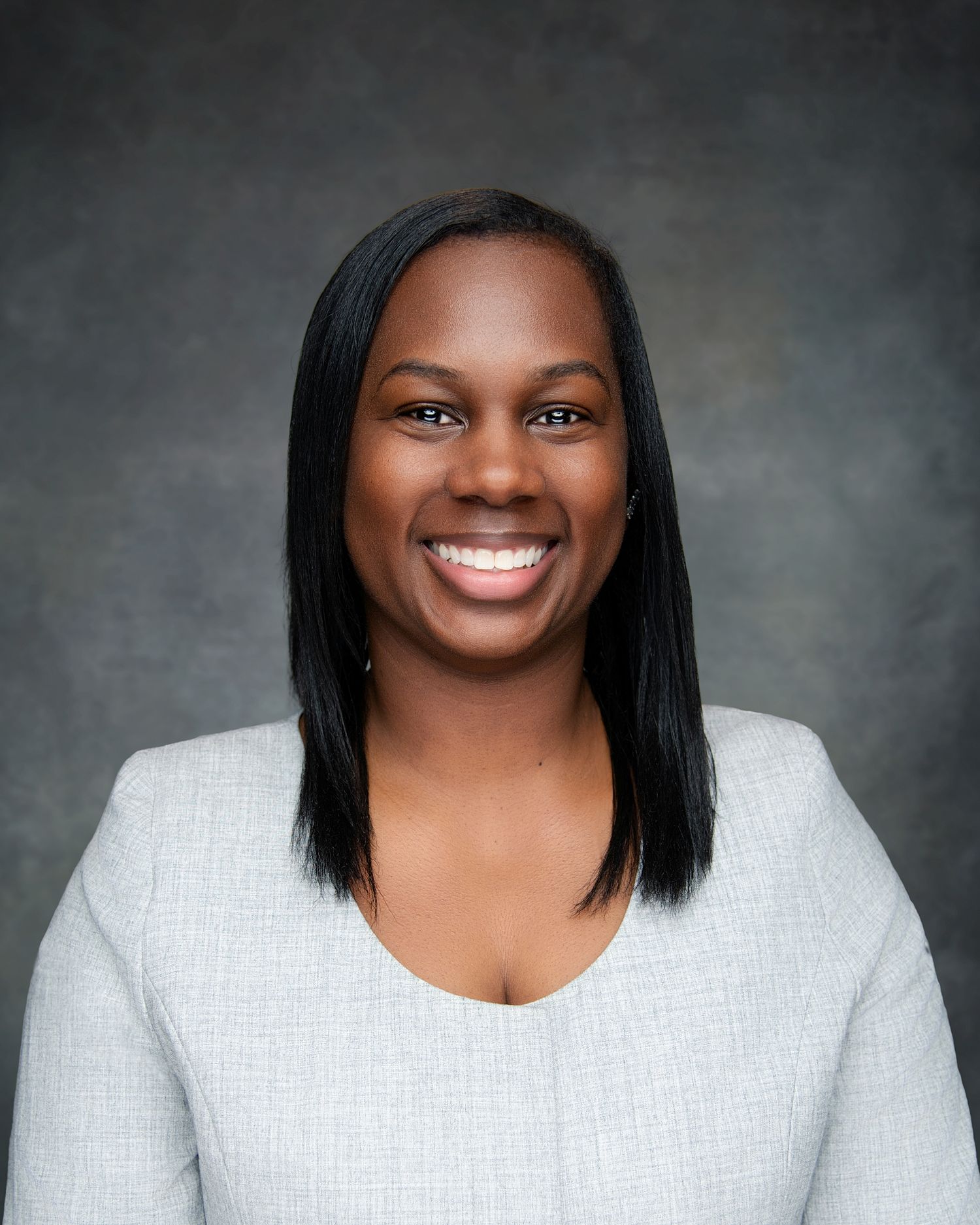 Professional headshot portrait of a person in a light gray sweater against a dark background, smiling warmly at the camera.