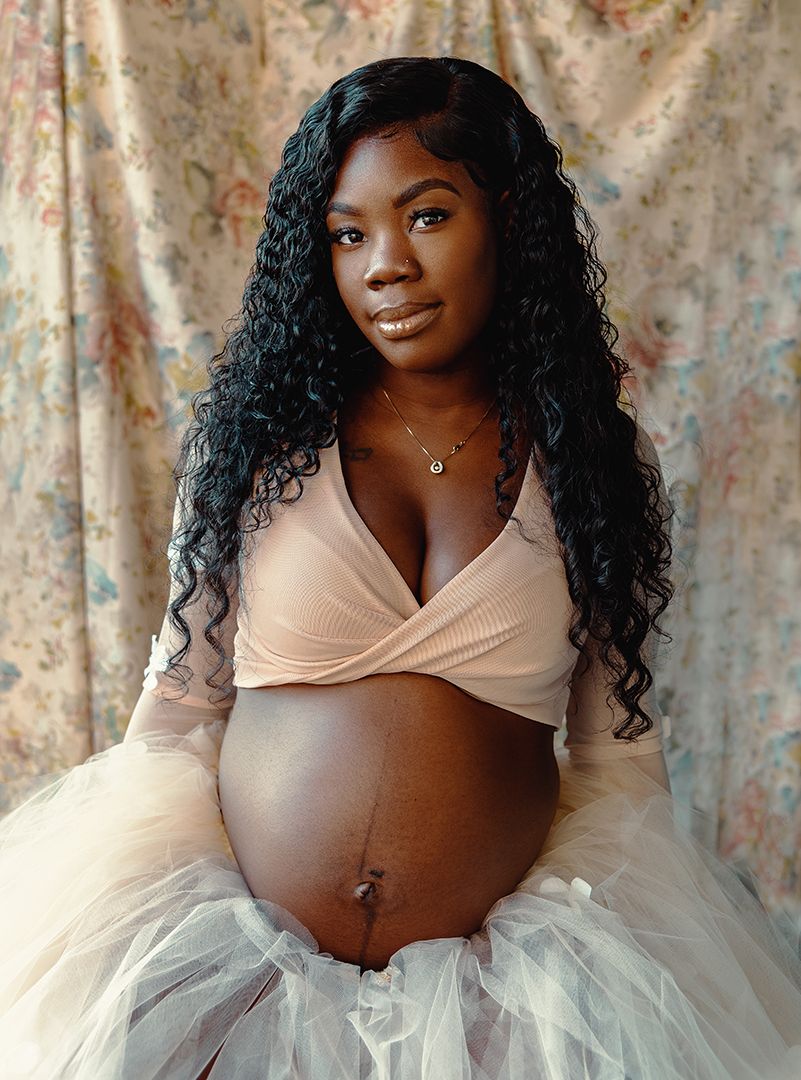Maternity photoshoot featuring a white tulle skirt and peach wrap top against a floral backdrop.