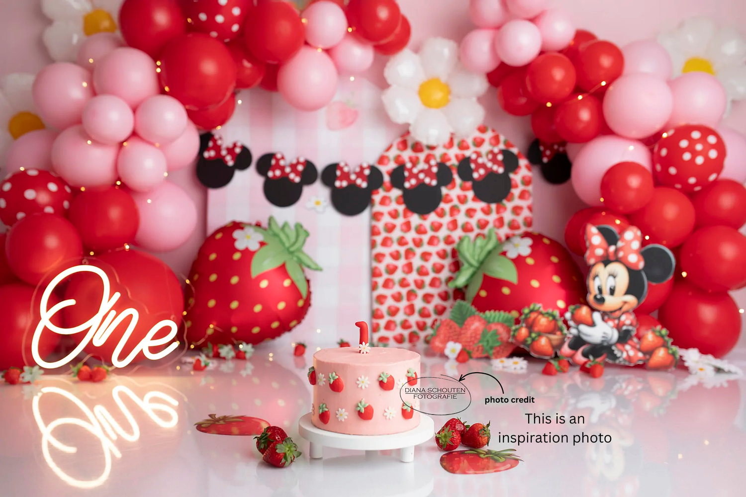 Minnie Mouse first birthday cake smash setup with red pink balloons strawberries neon One sign and themed decorations.