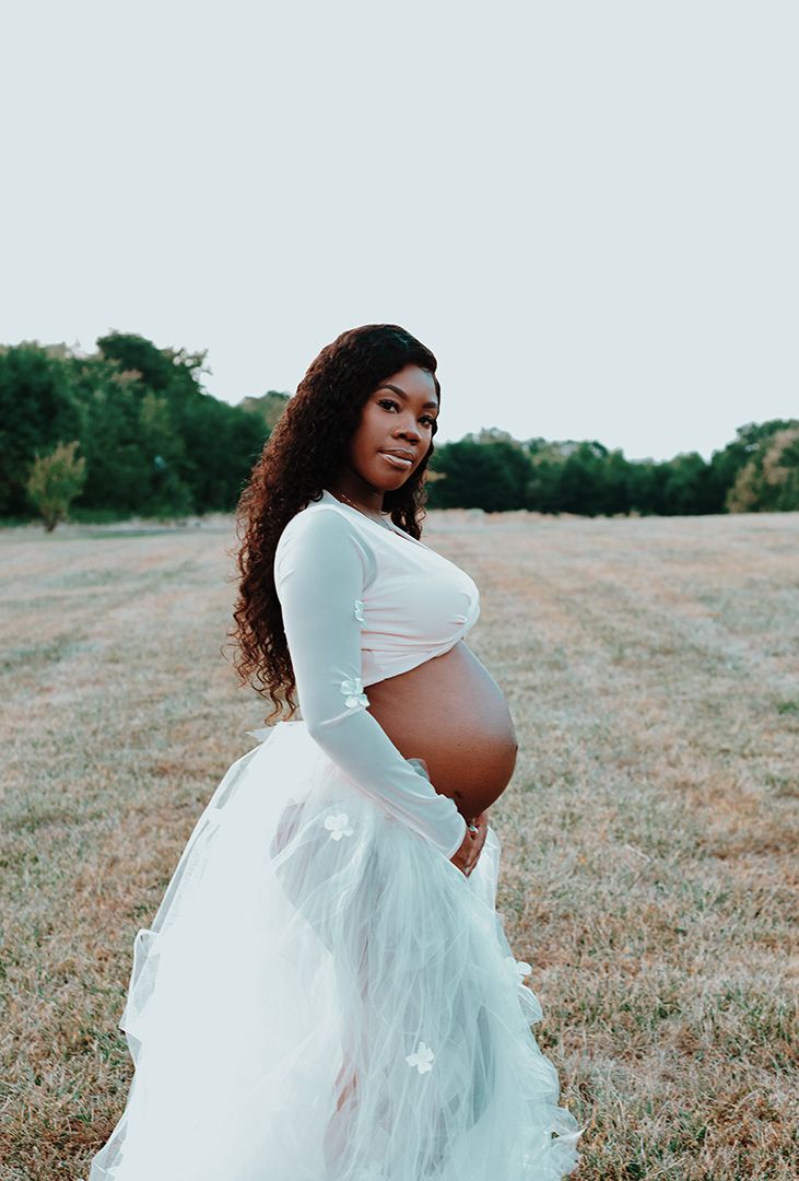Outdoor maternity session in a flowing white tulle dress against a natural field setting.