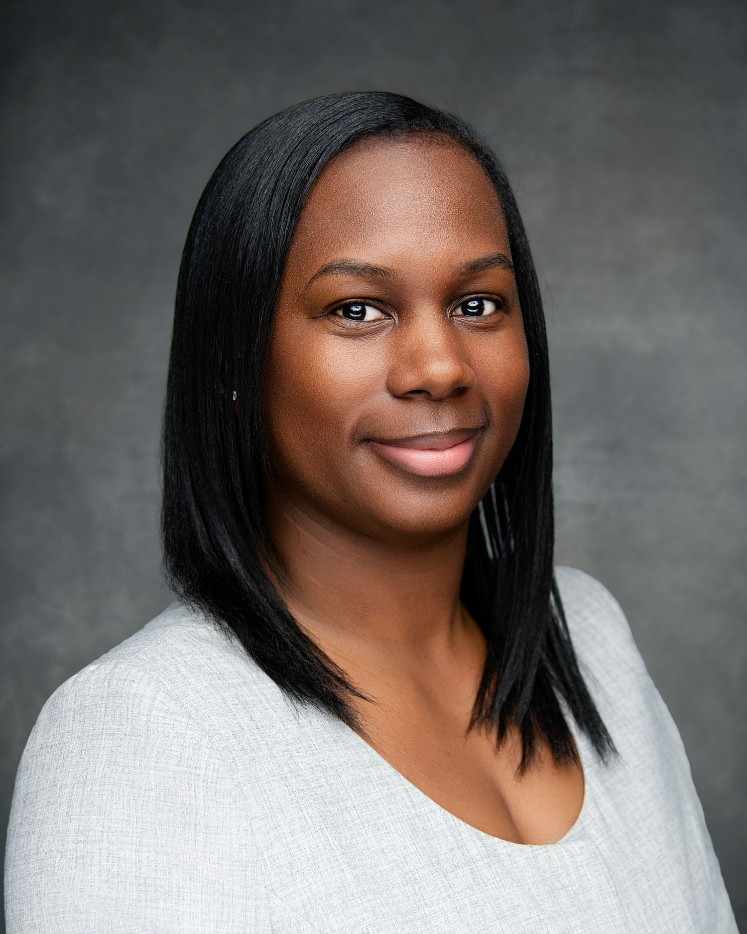 Professional headshot portrait of a person in a white sweater against a gray background with a warm smile.
