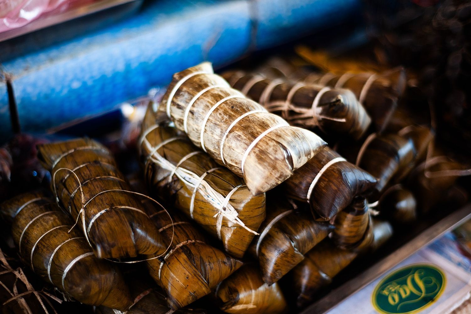 Rows of handmade traditional Chinese zongzi dumplings wrapped in bamboo leaves displayed on wooden surfaces.