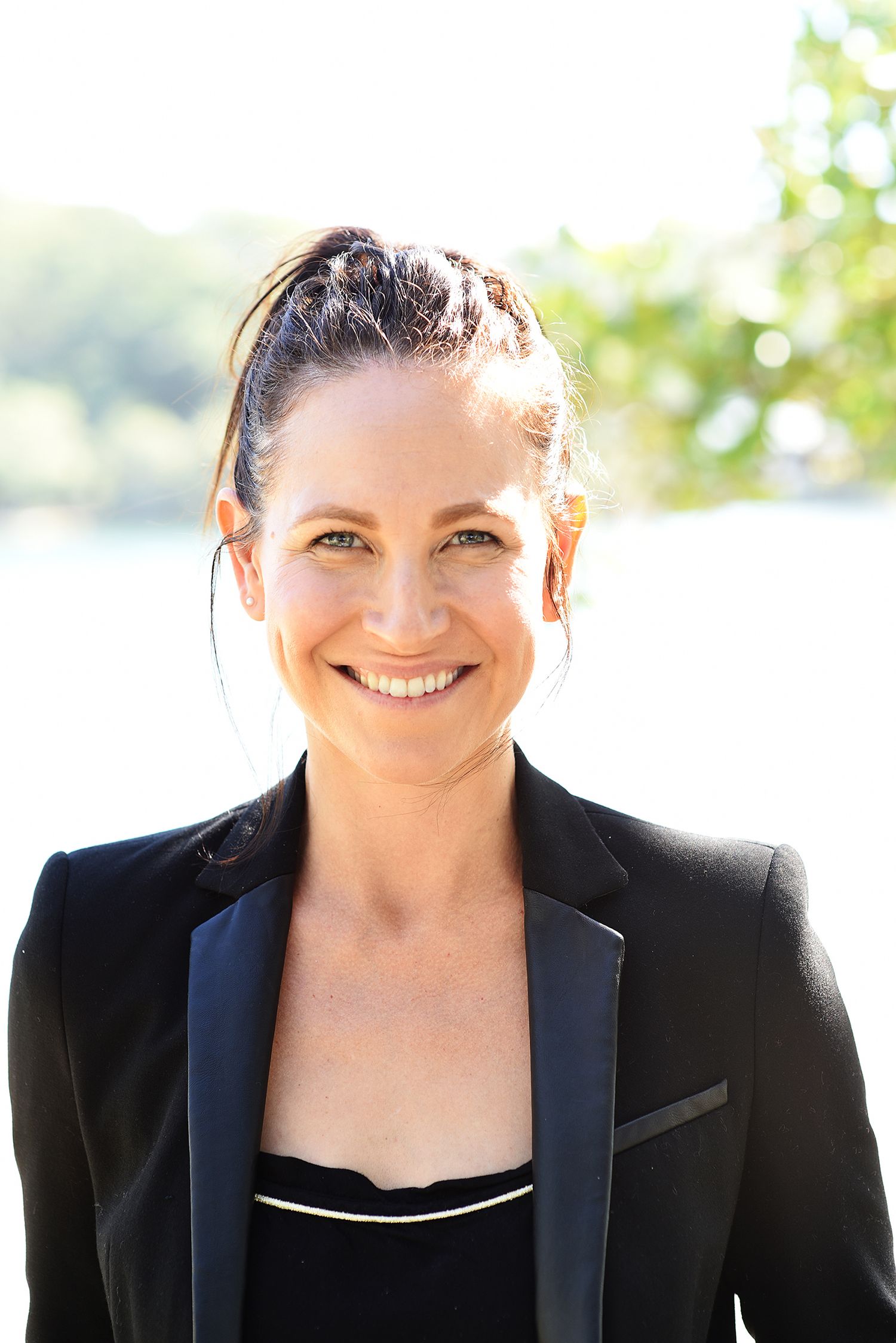 Outdoor portrait of someone in black blazer smiling warmly in natural sunlight.