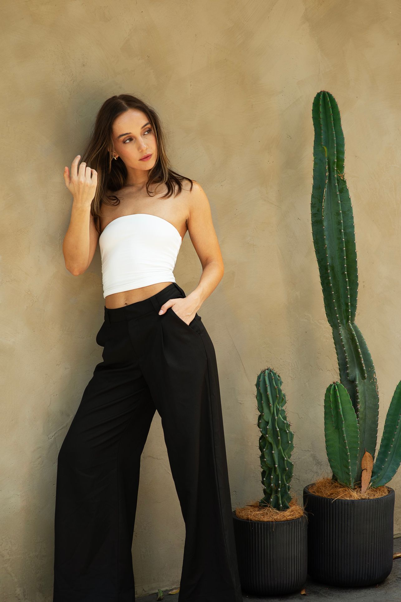 Fashion portrait series with black pants and white top against beige wall with decorative cacti.