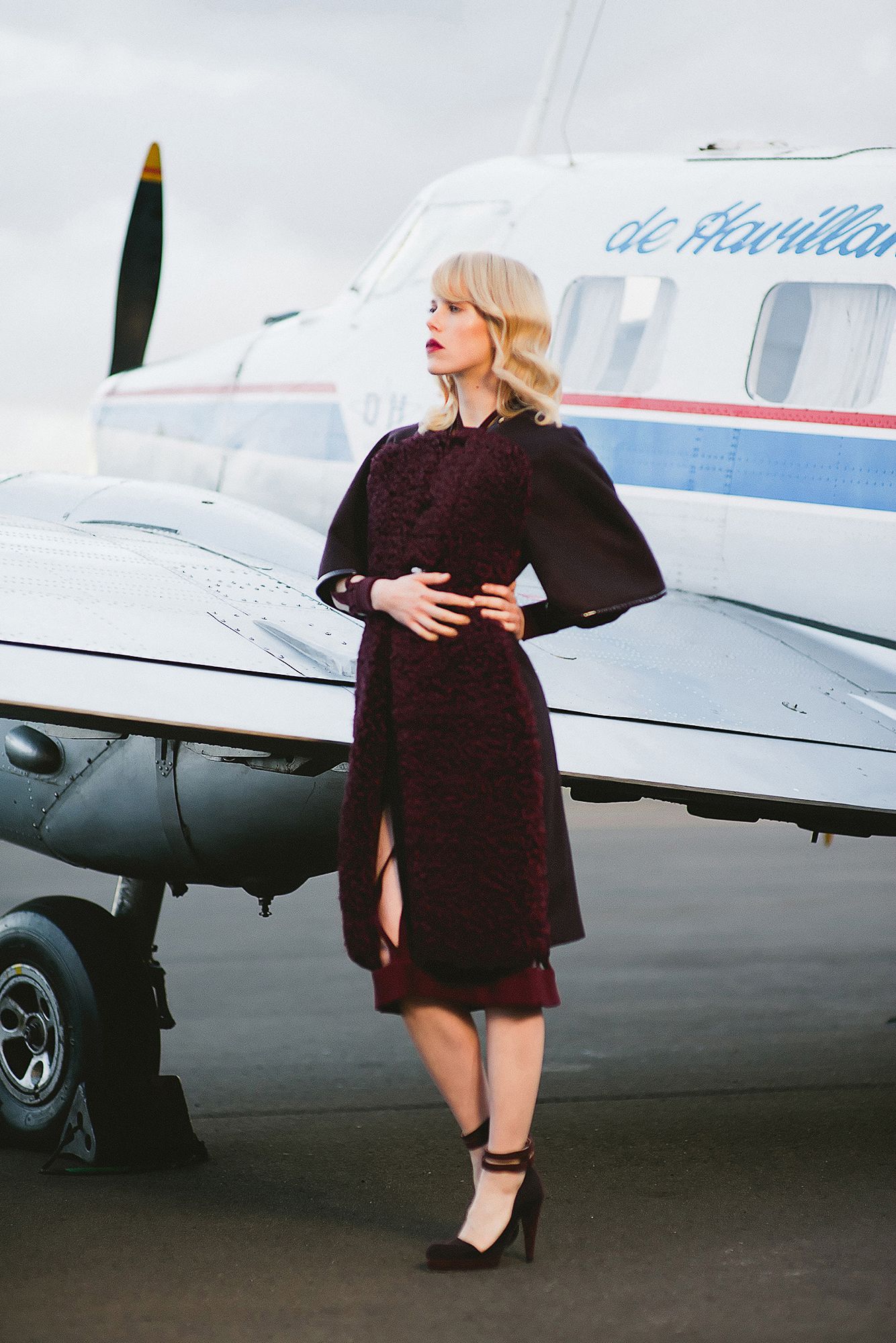 Fashion shoot near a small aircraft featuring a dark dress and dramatic poses.