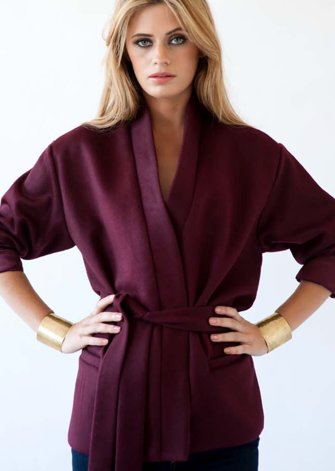 Fashion series showing burgundy structured jacket with gold cuff details against white background.