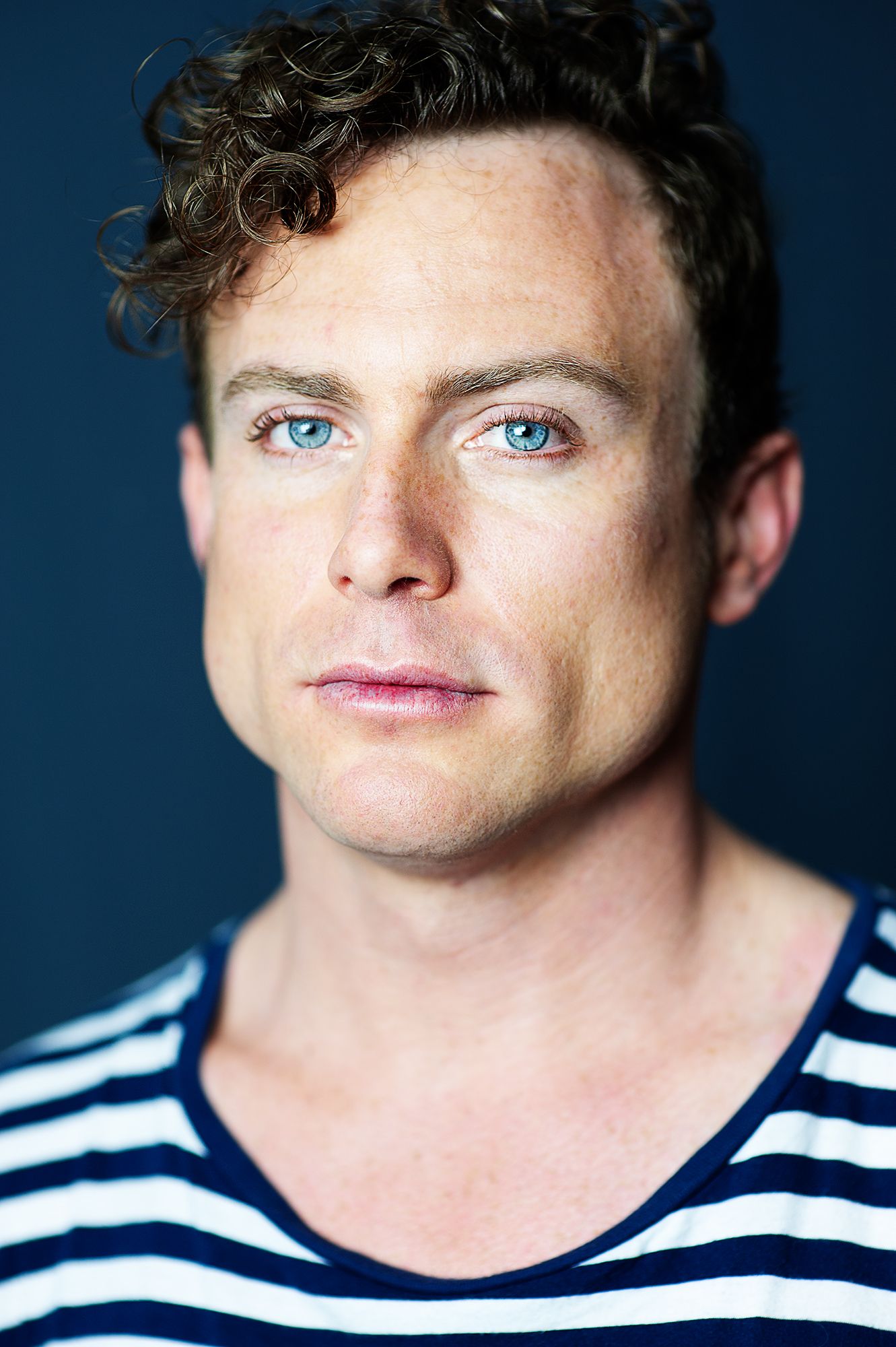 Close-up portrait with striped shirt against dark background.