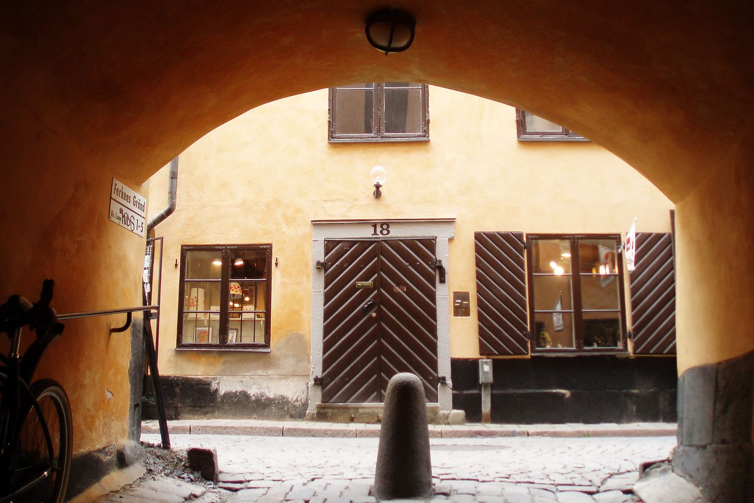 Arched passageway leading to a traditional European courtyard with yellow walls and wooden shuttered windows.
