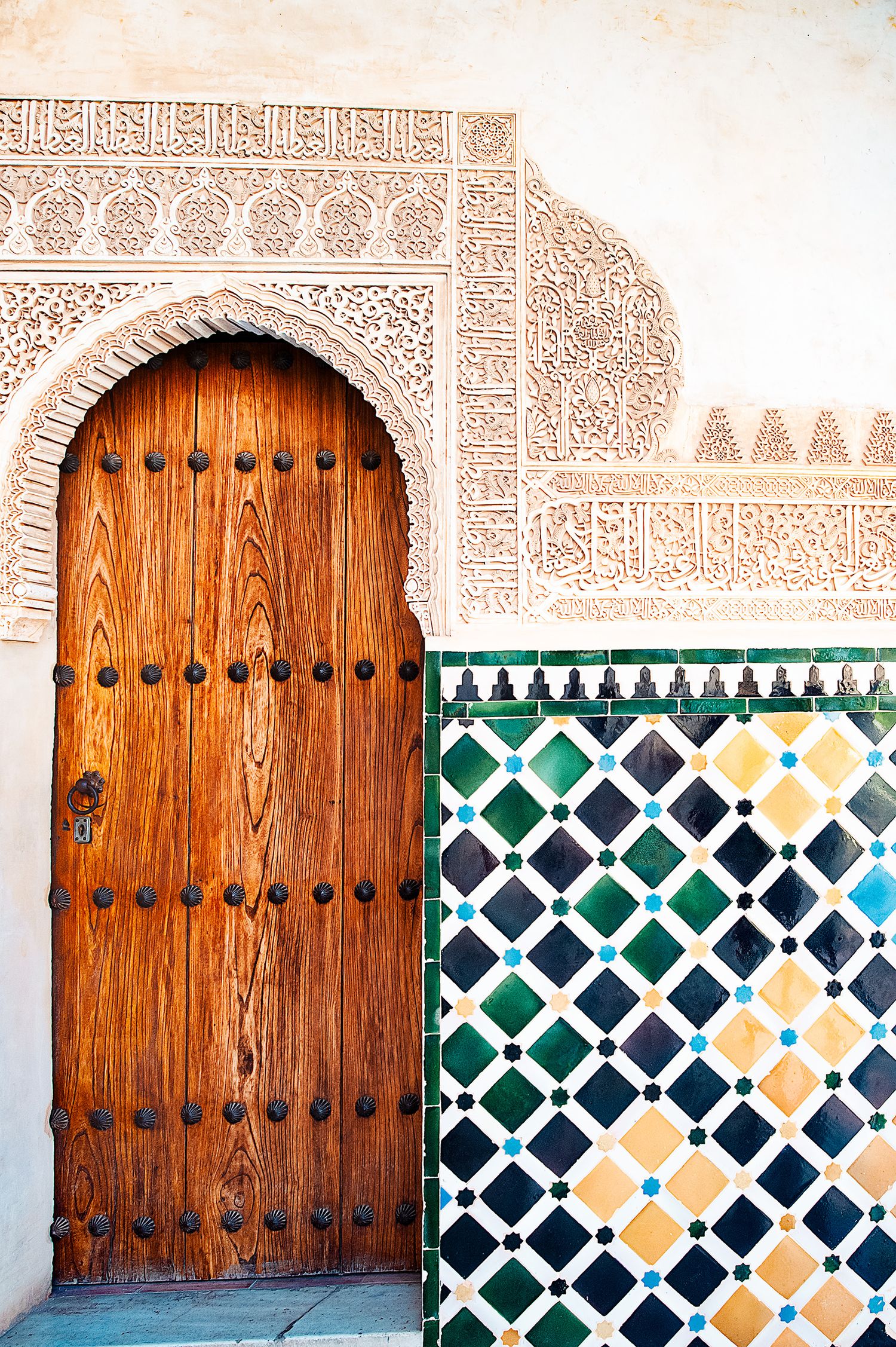 Ornate wooden doors with decorative tiles and Islamic patterns adorn the walls of the Alhambra Palace in Granada, Spain.