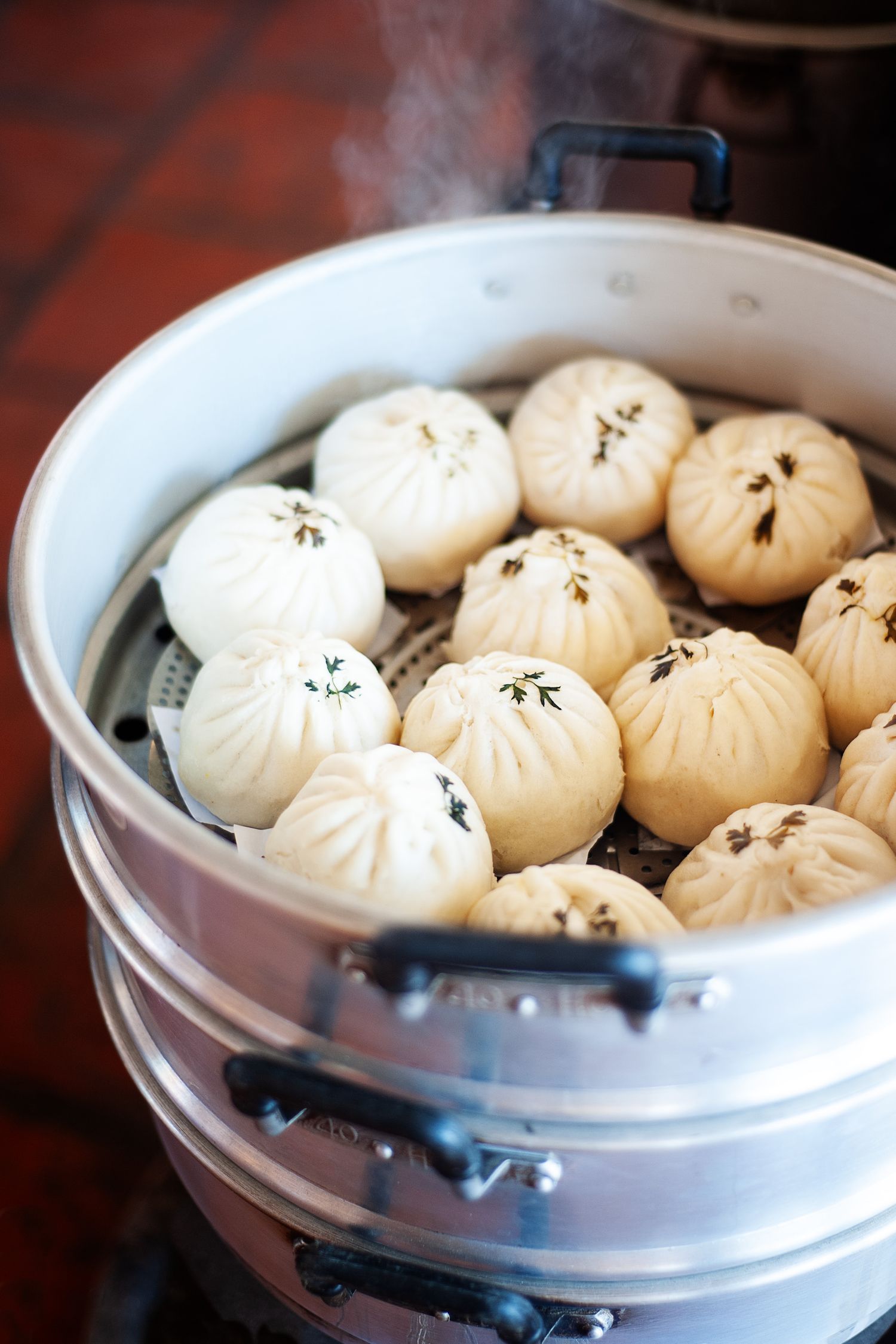 Steaming hot soup dumplings arranged in a white bamboo steamer basket.