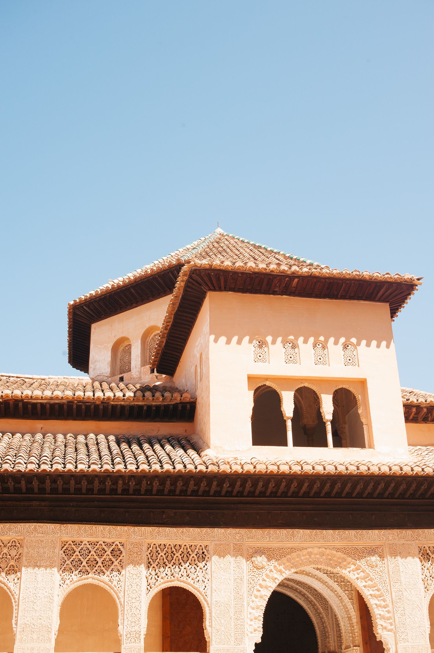 Architectural detail of the Alhambra palace showing ornate Moorish arches and terracotta roof tiles against a blue sky.