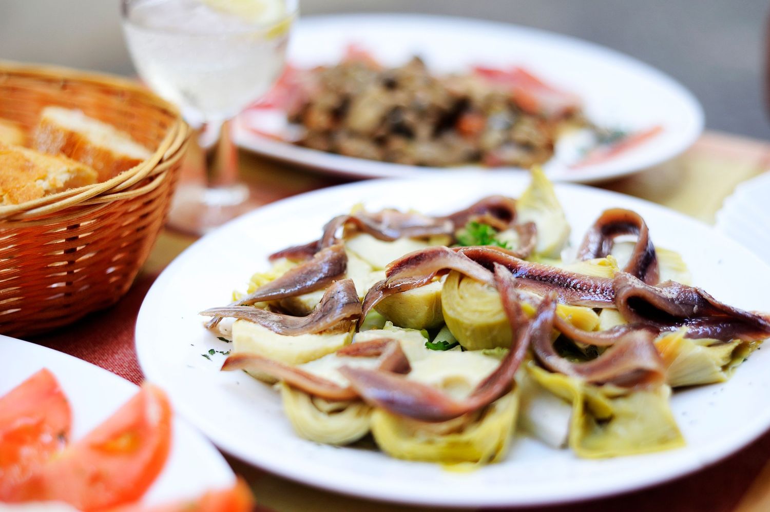 Fresh seafood appetizers and salad plates arranged on a restaurant table with bread basket and garnishes.