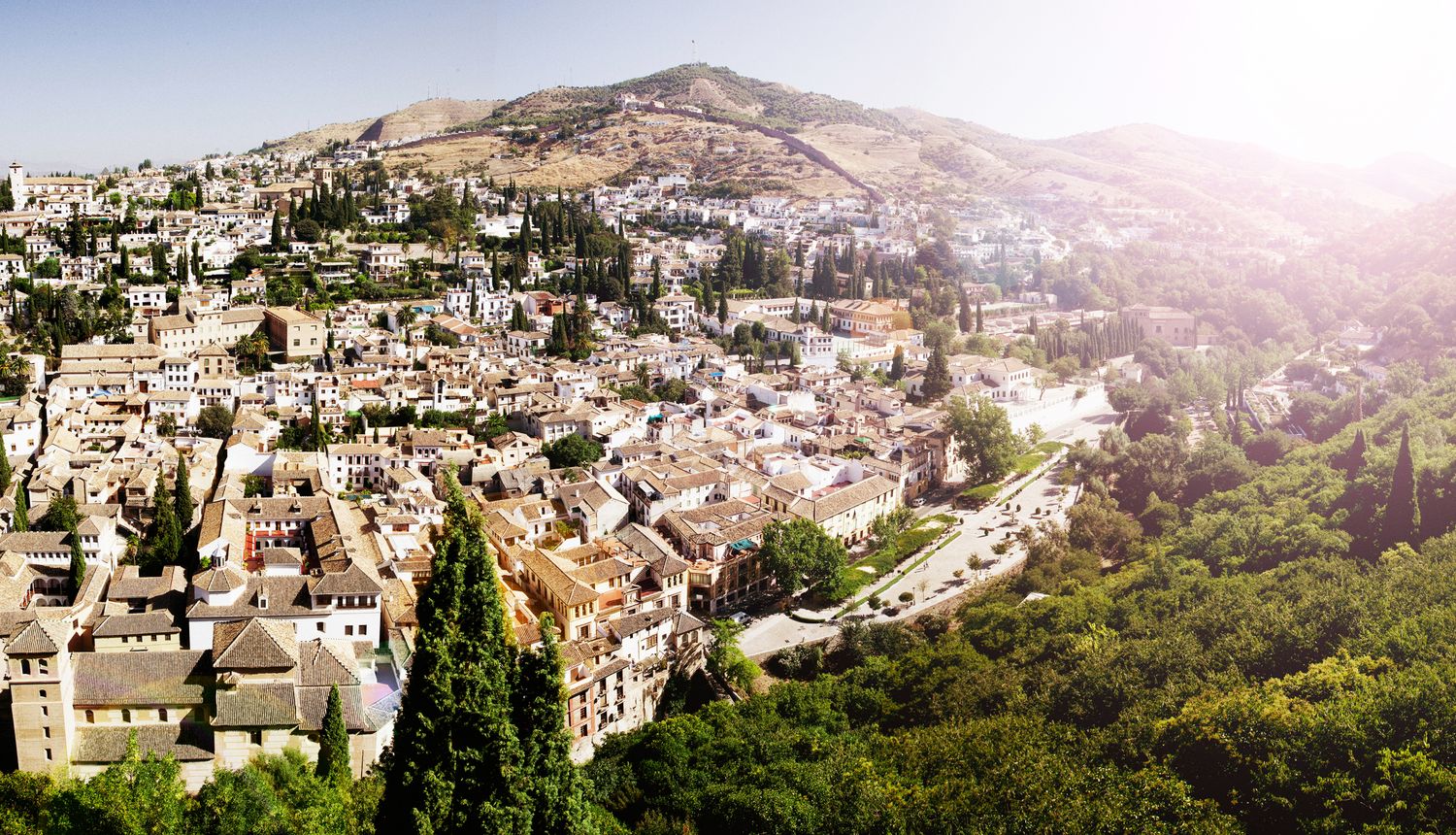 Panoramic view of Granada's historic Albaicin neighborhood with whitewashed buildings nestled in the hillside under sunlight.