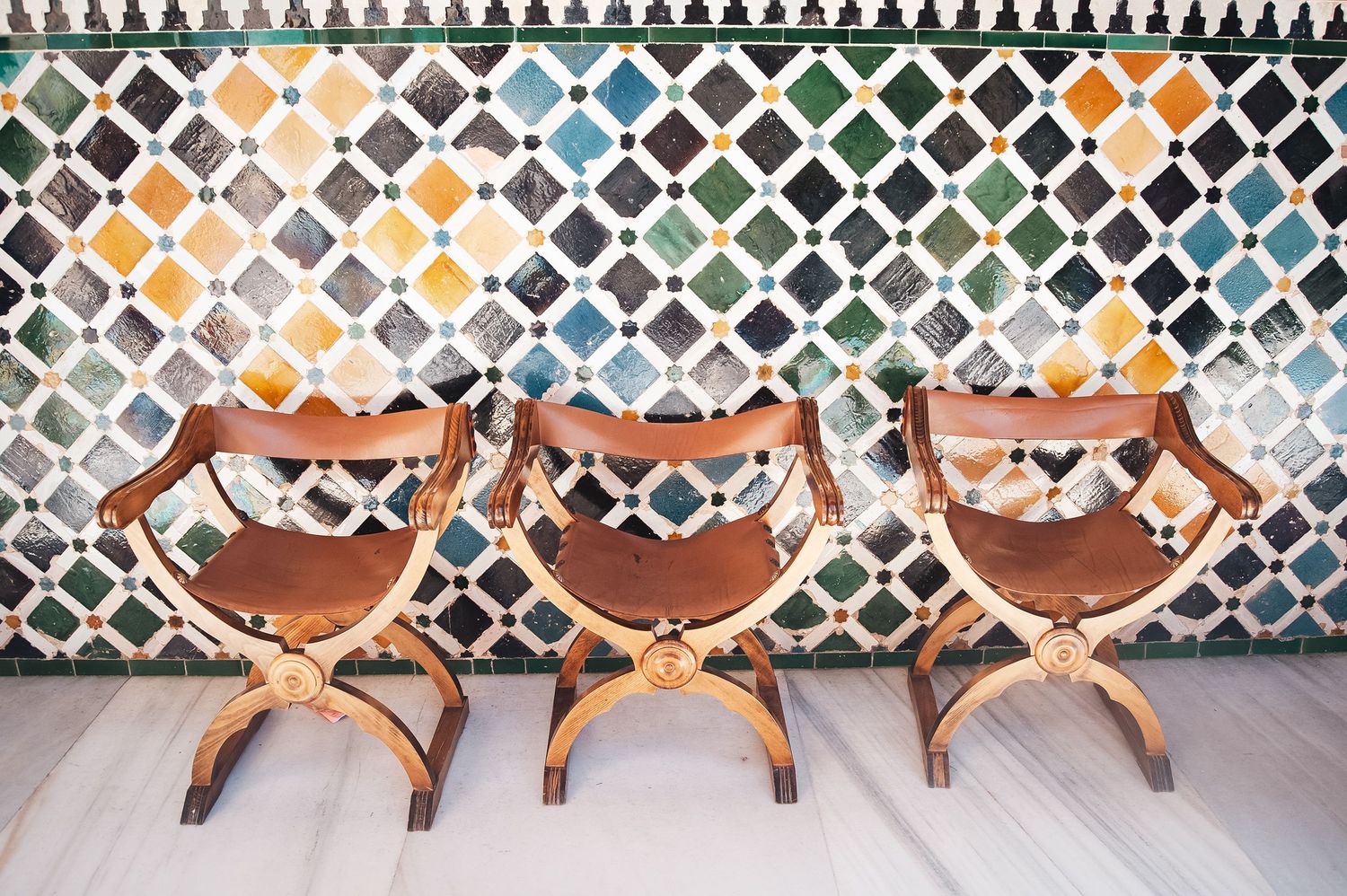 Three brown wooden chairs with curved backs sit against a decorative patterned wall in a row.