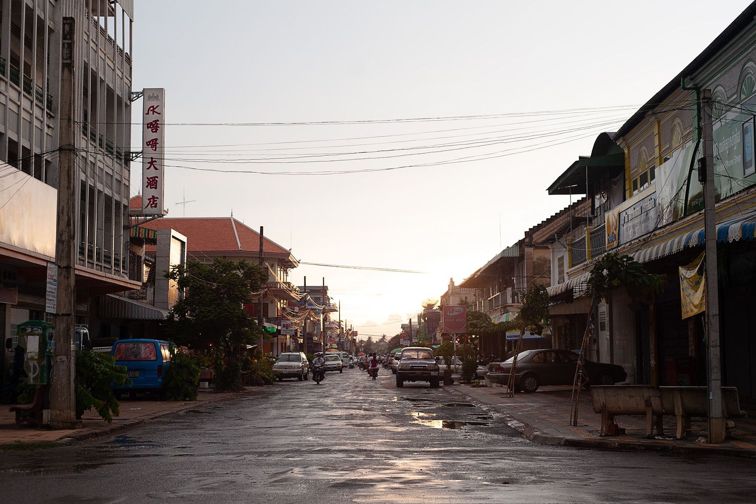A scene showing an empty road and buildings at dusk with power lines overhead.
