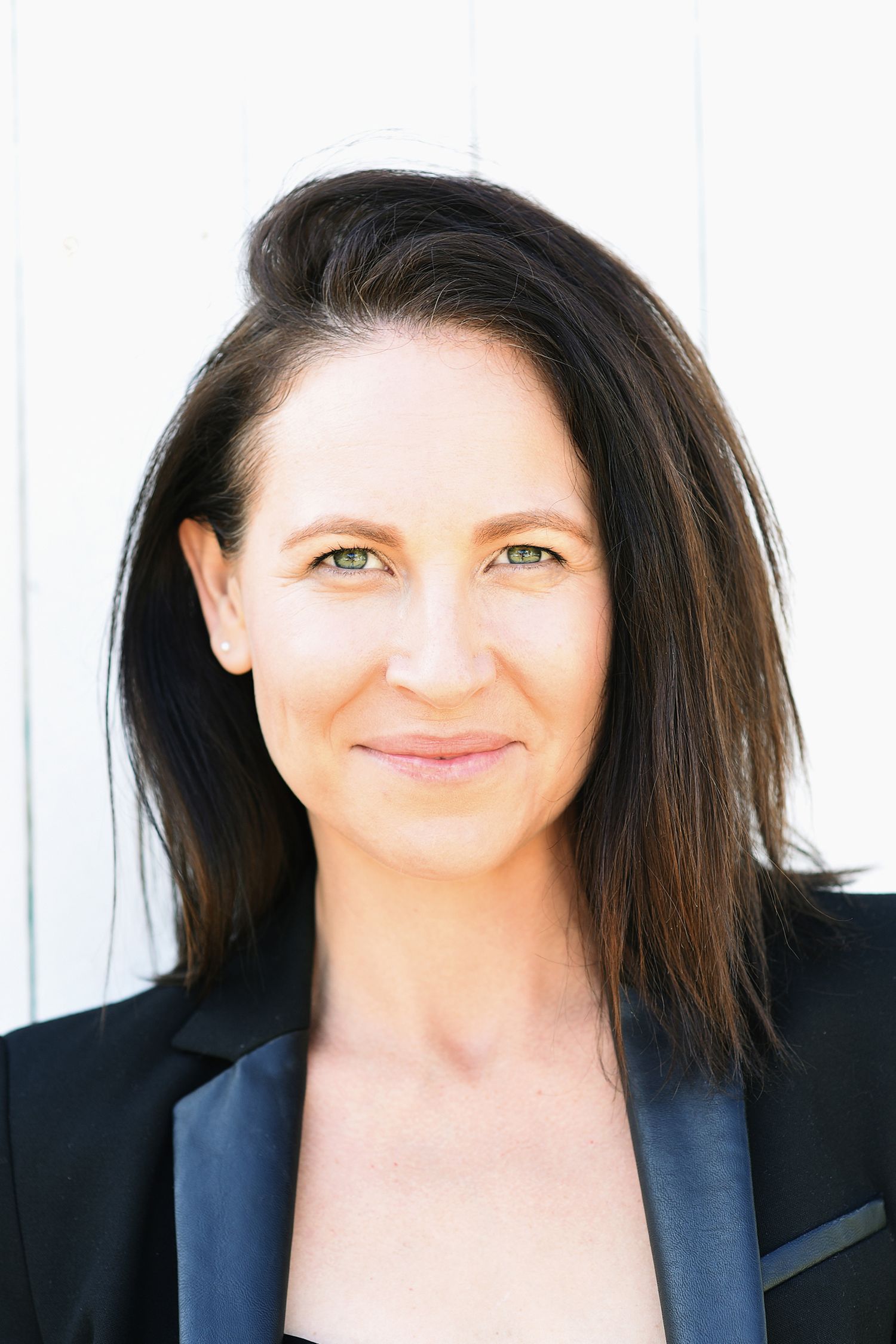 Professional headshot of someone in a black blazer with dark hair against white background.